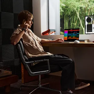 A person using a Googlebook laptop in a music studio, with a music production app open on screen.