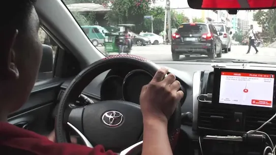 Interior view of a Toyota vehicle with a driver's hand on the steering wheel, showing a mounted tablet running a navigation app on the dashboard.