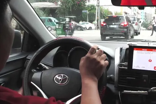 Interior view of a Toyota vehicle with a driver's hand on the steering wheel, showing a mounted tablet running a navigation app on the dashboard.