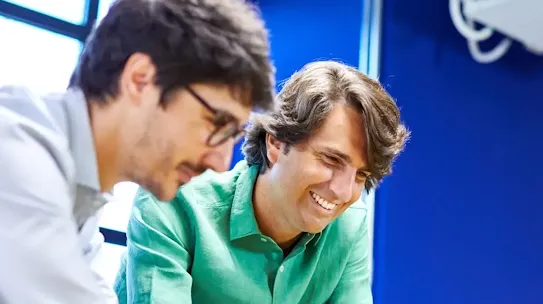 A smiling man in a green shirt from down with a colleague.