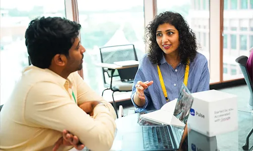 A woman and a man engaging in conversation while looking at a laptop screen.