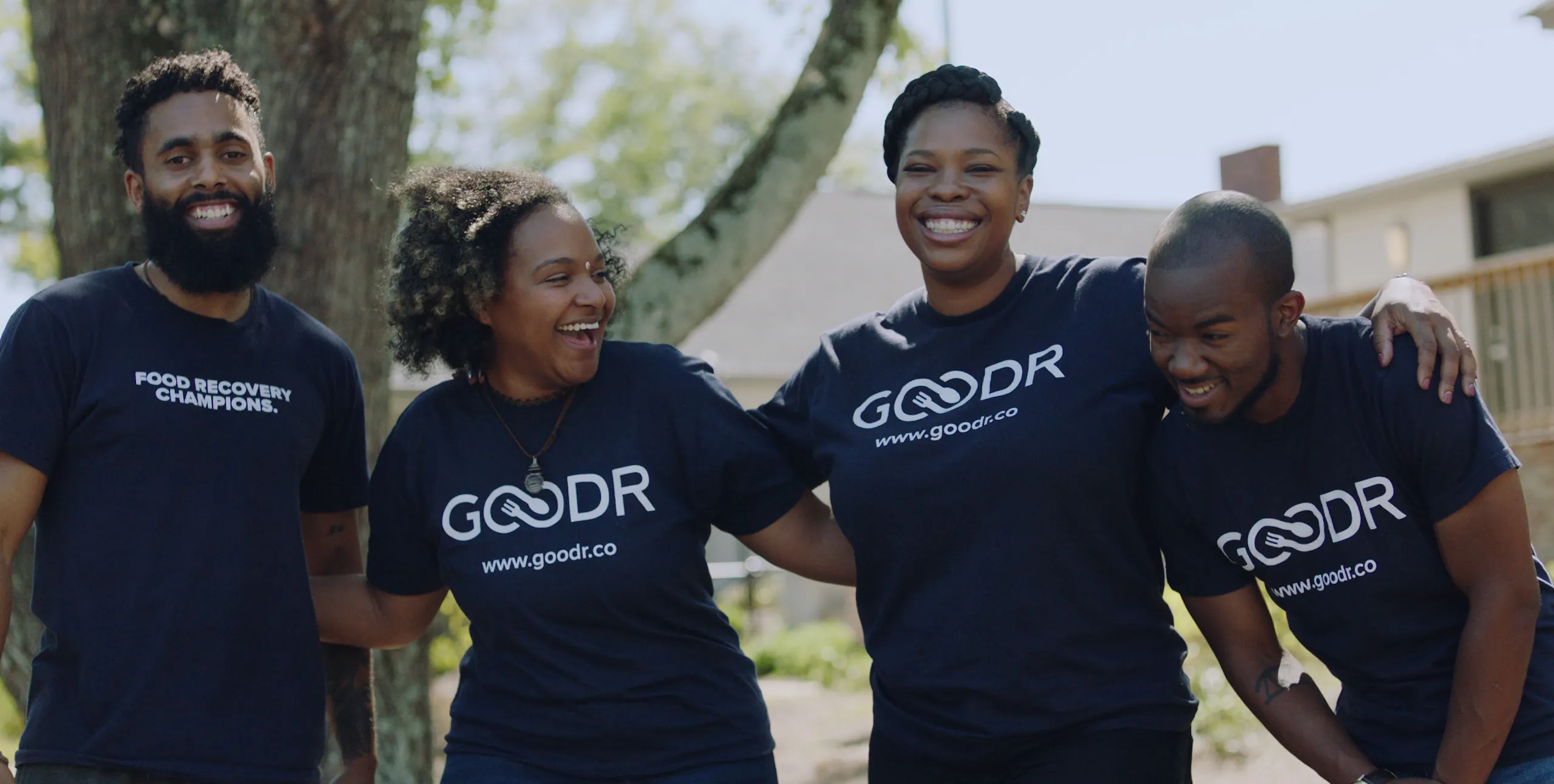 Group of coworkers wearing matching shirts smiling and holding shoulders