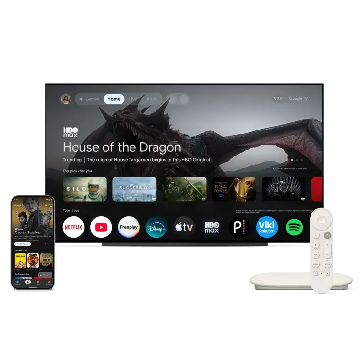 TV displaying the Google TV user interface Home screen. Sitting in front of the TV are a smartphone displaying the Google TV app and a Google TV Streamer device.