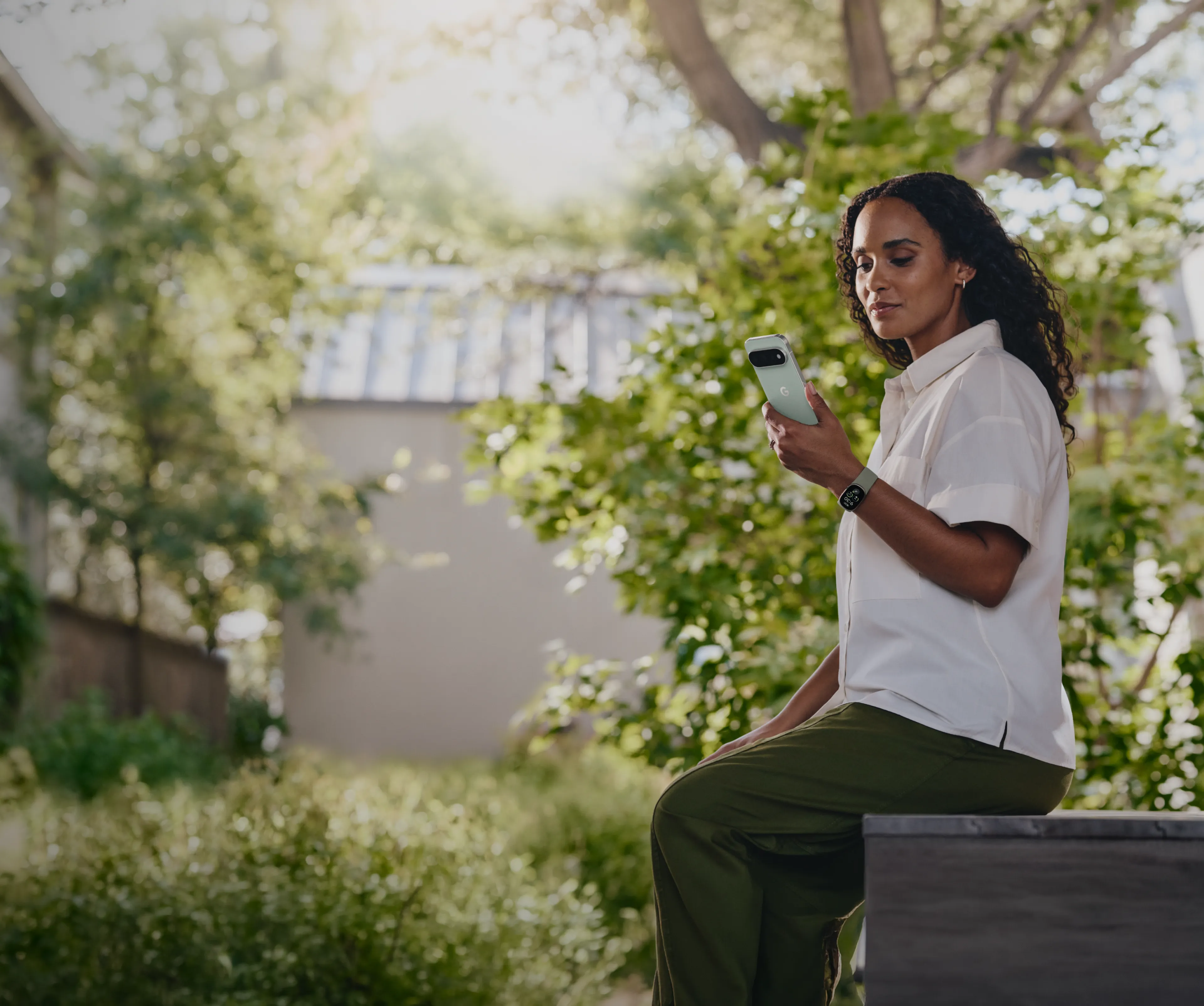 Image of woman sitting on couch, drinking coffee, and reviewing her stats in the Google Health App. 